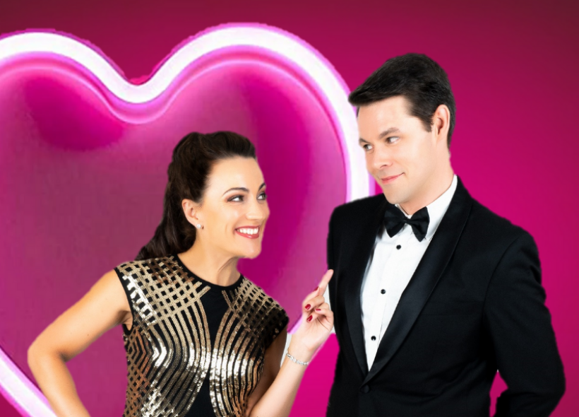 Karla Hillam and Jonathan Guthrie Jones wearing formal attire in front of a neon pink heart sign.