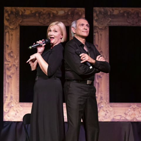 Corinne Andrew & Milko Foucault-Larche performing on stage in all black attire with vintage picture frames in the backdrop.