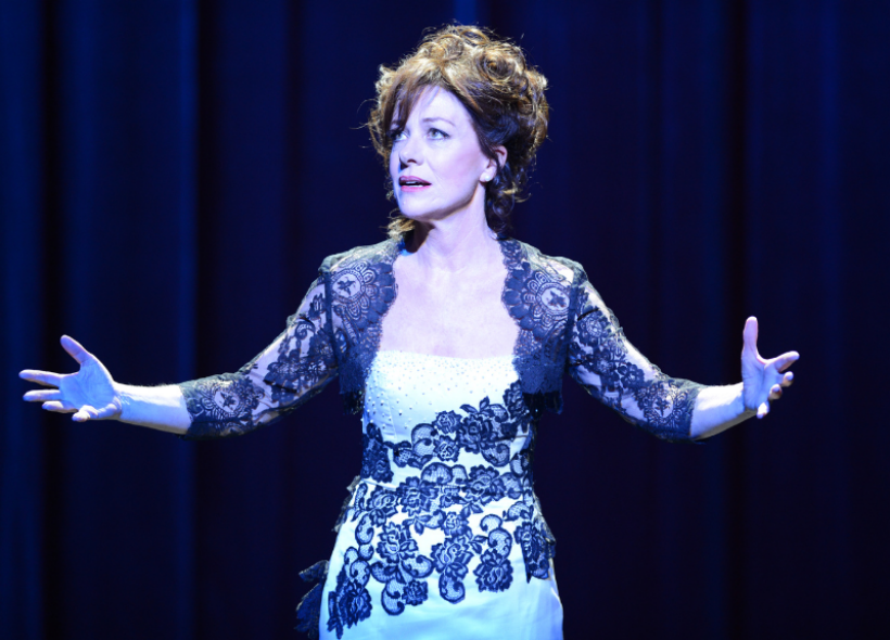 Bernadette Robinson in a blue dress performing on stage with her hands raised by her side.