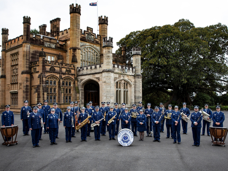 NSW Police Band standing with their instruments in uniform in front of a large castle.