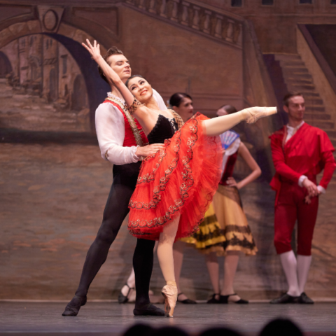 Man and a woman in a red dress dancing in the ballet on stage