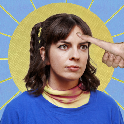 A woman with brown hair in pigtails looks serious while a hand extends from the right side of the image, with its index finger pointing at her forehead. The background features a circular yellow halo with sun rays radiating from it against a blue backdrop.