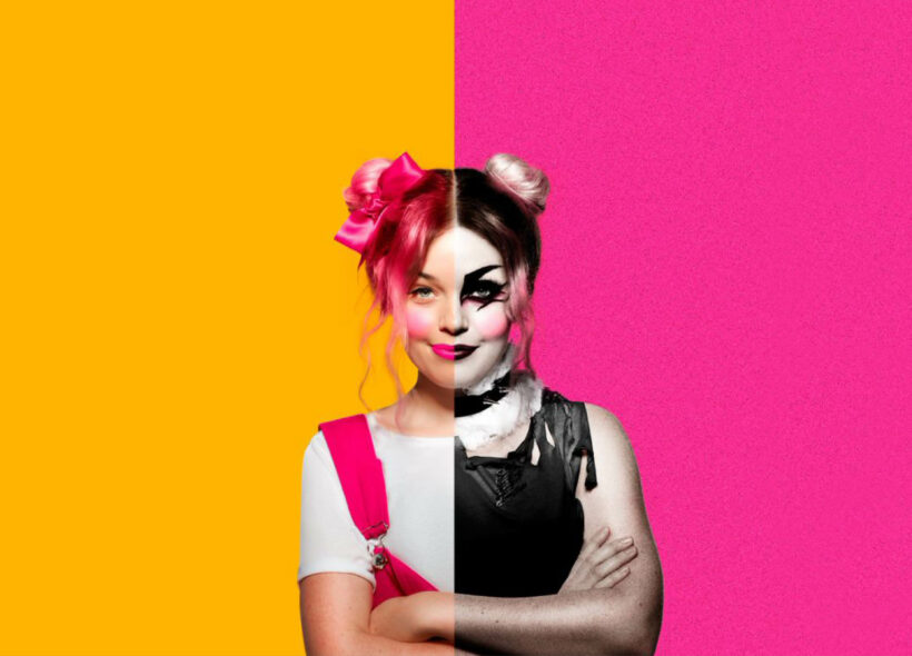 A young woman stands with arms crossed. The image is split in two - in the left it has a yellow background and she has pink hair and overalls - on the right it has a pink background and she has a black goth make-up look.