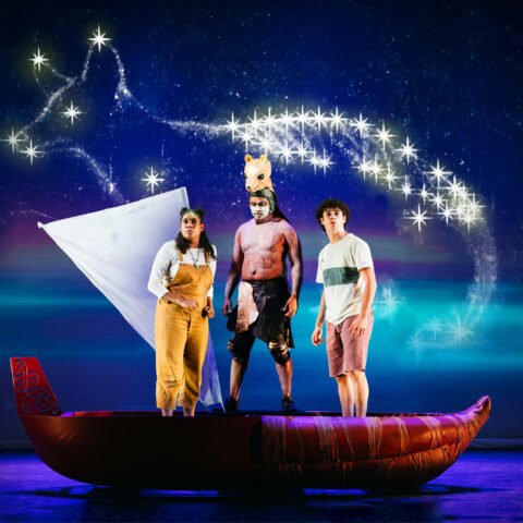 Three First Nations people stand in a small red boat with a white sail. In the night sky behind them is the shape of a Tasmanian tiger made out of stars. 