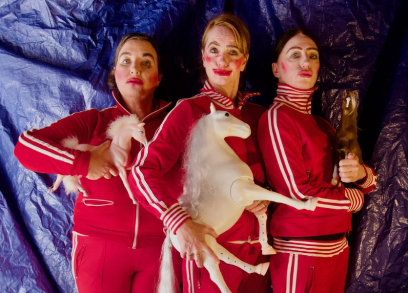 Three women dressed in tracksuits holding miniature horse dolls.