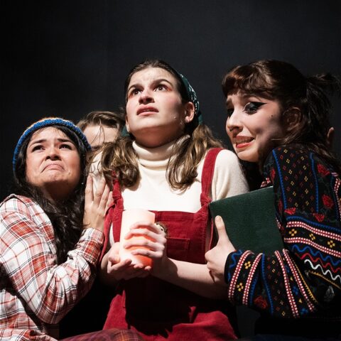 Three characters of the show looking scared, one on the left dressed in red flannel, one in the middle dressed in a white shirt and red overalls and one on the right dressed in a black Christmas jumper.