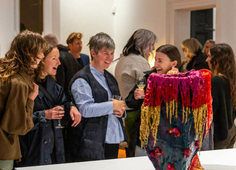 Photo taken on Design Fringe 2023 Opening Night. Four people stand around the exhibiting art vase and smile with each other. 