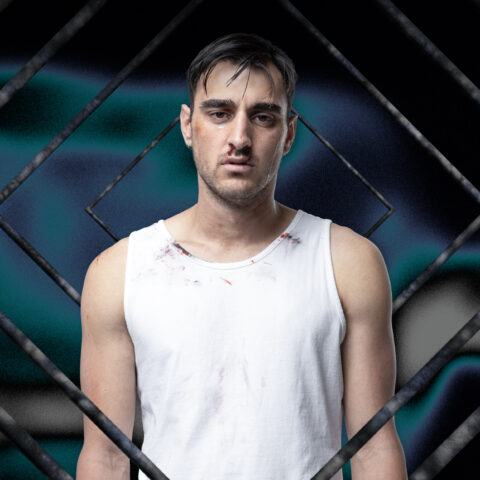 A young white man with dark hair and bold eyebrows stares wistfully at the camera. He's on a warped moss green and black background and is surrounded by graphic rectangles. He wears a bloodied white singlet.