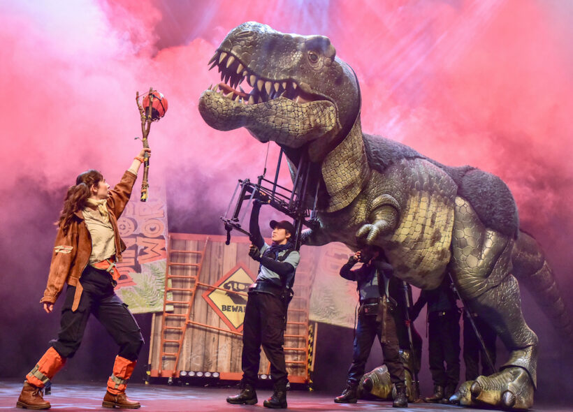 A production image of explorer Miranda facing off against a life-size T-Rex puppet