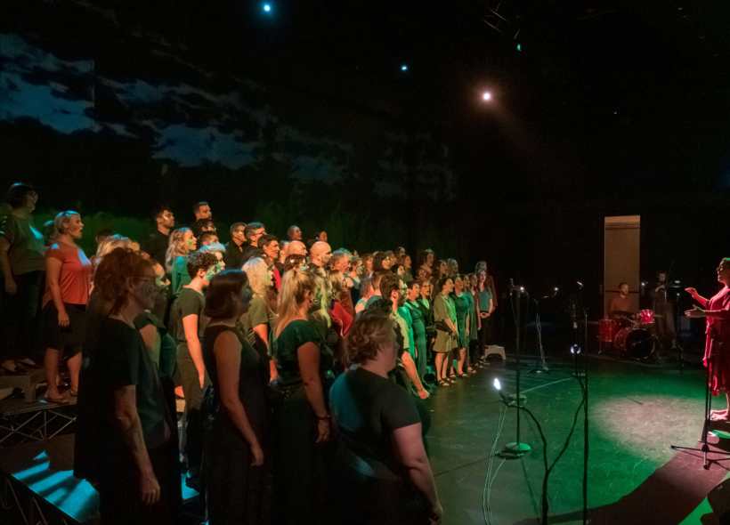 The singers of the Menagerie choir perform under a dreamy green light, a darkened skyscape behind them. 