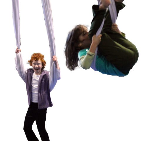 Two teenagers swinging on circus silks which hang from the roof