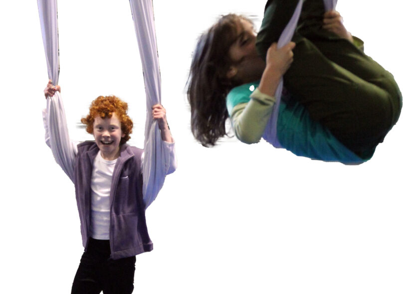 Two teenagers swinging on circus silks which hang from the roof