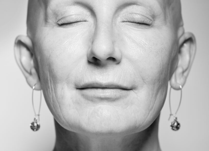 Black and White image of a women with her eyes closed and a shaved head 