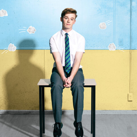 Young boy with red hair sitting on a bench alone in front of a blue and yellow backdrop