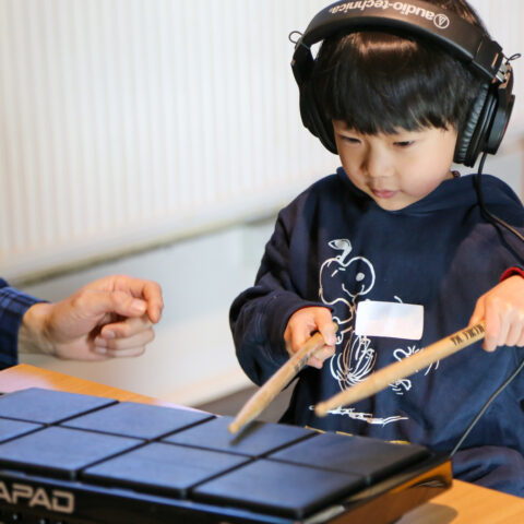 Young person playing electronic instrument while listening through headphones.