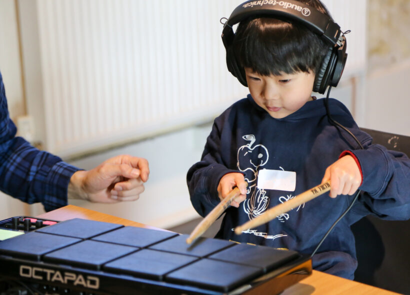 Young person playing electronic instrument while listening through headphones.