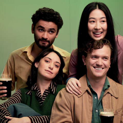 Four friends smiling with two holding beer