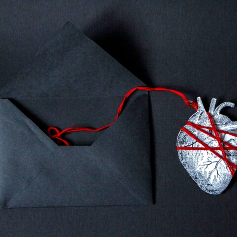 Heart wrapped in red string coming out of a black envelope