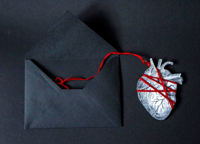 Heart wrapped in red string coming out of a black envelope