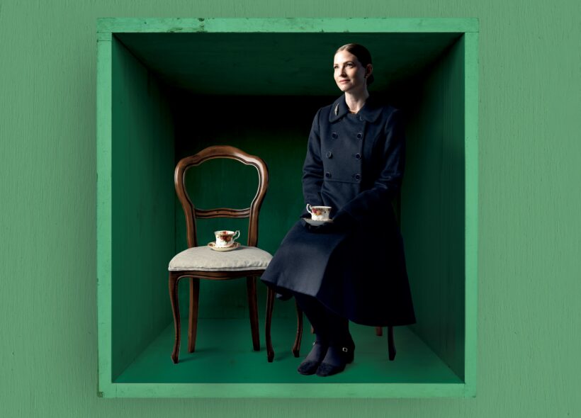 Elizabeth Blackmore sitting on a chair, holding a cup of tea looking into the distance. 