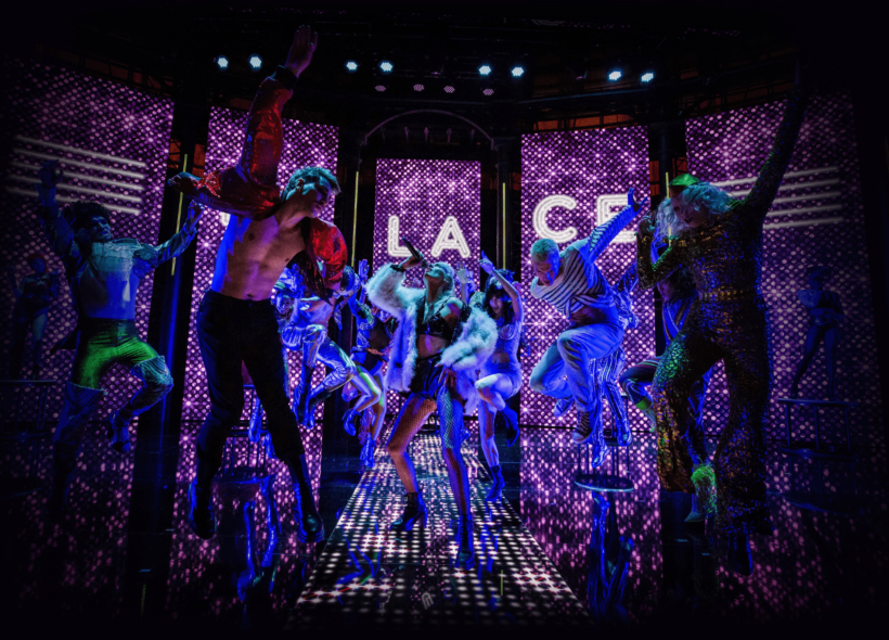 Decked out in multicolour fashion, a singer is centrestage mid-note and surrounded by Parisian dance troupe of eight, mid-dance on fashion runway