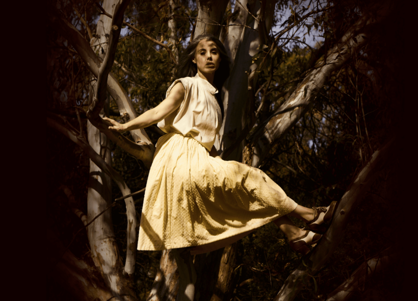 Young woman in lemon yellow dress and vintage shoes posing in Eucalyptus tree overlaid with dappled light and shadows 