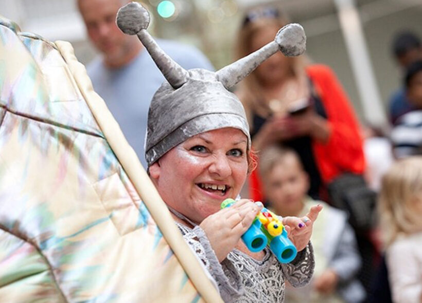 Caroline Bowditch wearing a silver alien-like headpiece and holding binoculars.