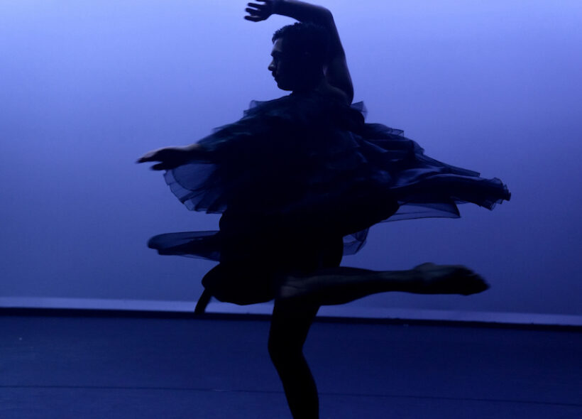 A silhouette of a woman gracefully dancing in a flowing black dress against a soft, illuminated background.