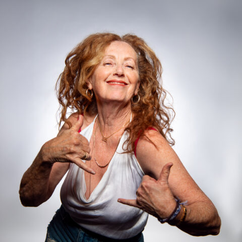 A woman with long, curly hair in a white tank top, showcasing a vibrant and cheerful demeanor.