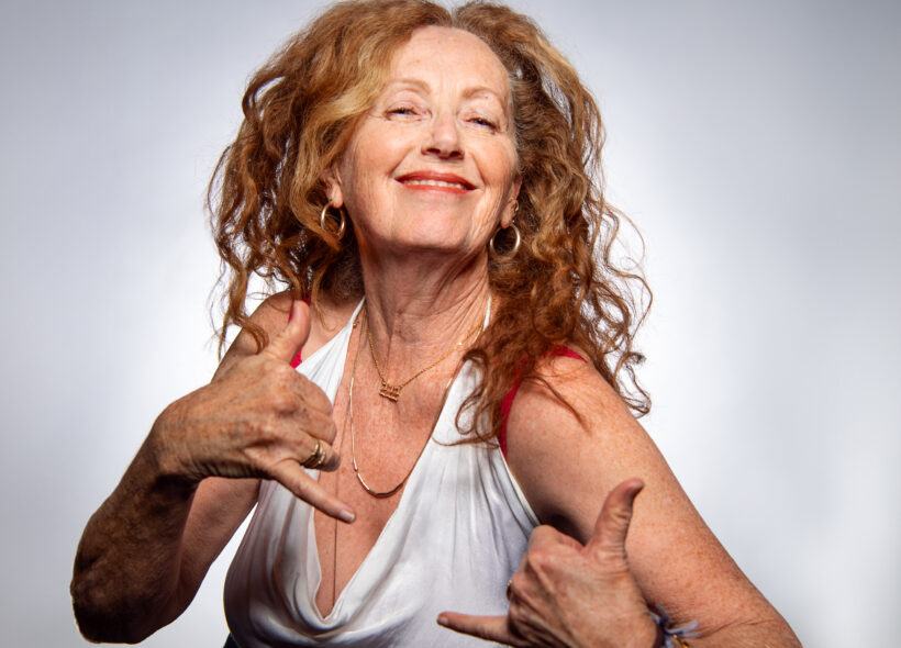 A woman with long, curly hair in a white tank top, showcasing a vibrant and cheerful demeanor.