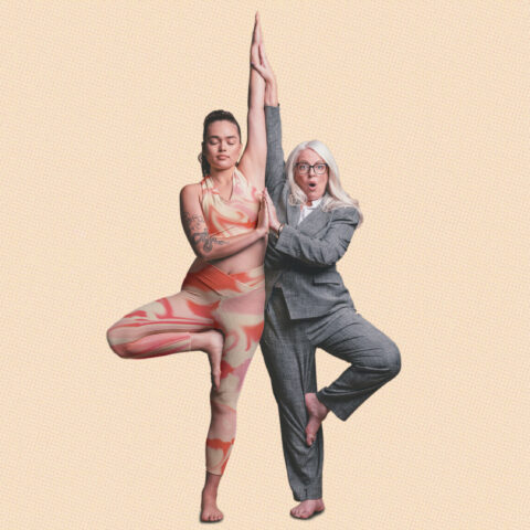 A mid-20s woman in activewear and an older lady in a grey suit complete a yoga pose together