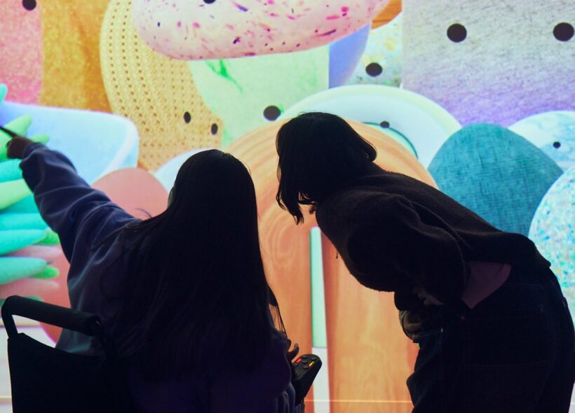 Two visitors, one in a wheelchair, in front of an artwork in Beings