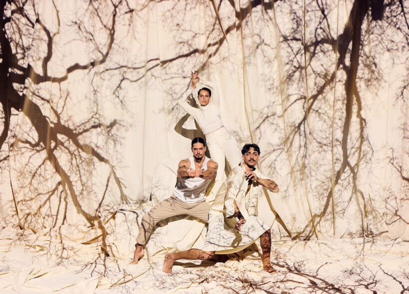 Two men one woman dynamically posing in neutral clothing against a cream background with projection of tree branches on them