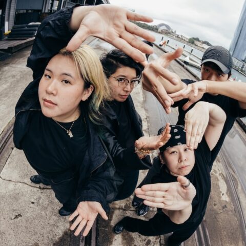 Four female street dancers wearing black , all with their hands raised up to the camera 