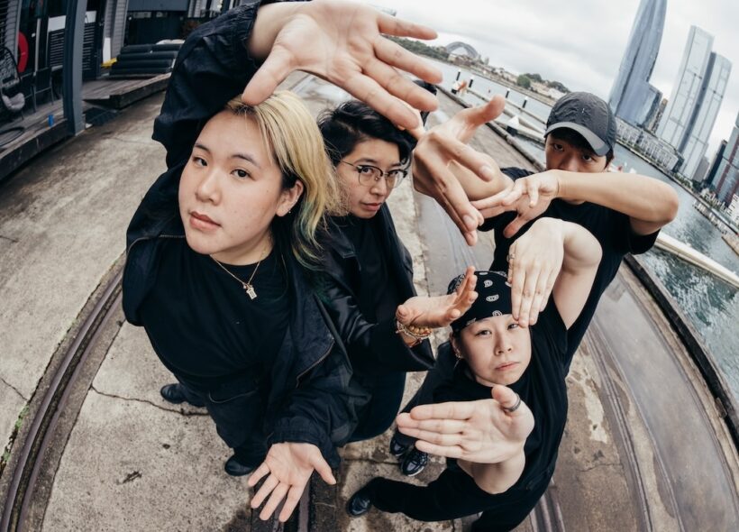 Four female street dancers wearing black , all with their hands raised up to the camera 