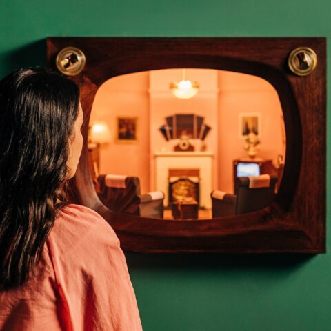 A visitor at The Story of the Moving Image Exhibition looking into a miniature loungeroom set.