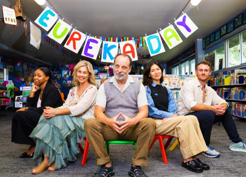 The cast of Eureka Day sit on children stairs in a classroom. 