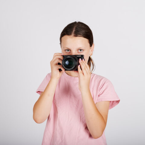 girl with brunette hair wearing a pink t-shirt holding a black camera