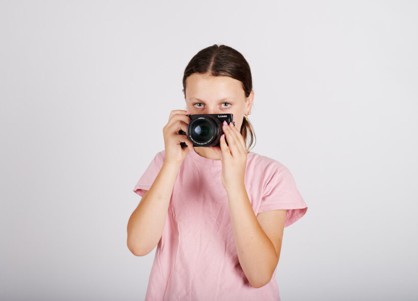 girl with brunette hair wearing a pink t-shirt holding a black camera