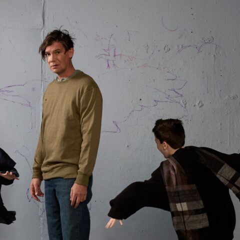 Standing man with two young bows dressed in black running circles around him
