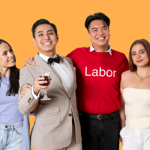 Four people smiling together against an orange background; one wears a “Labor” shirt, another holds a glass of red wine.