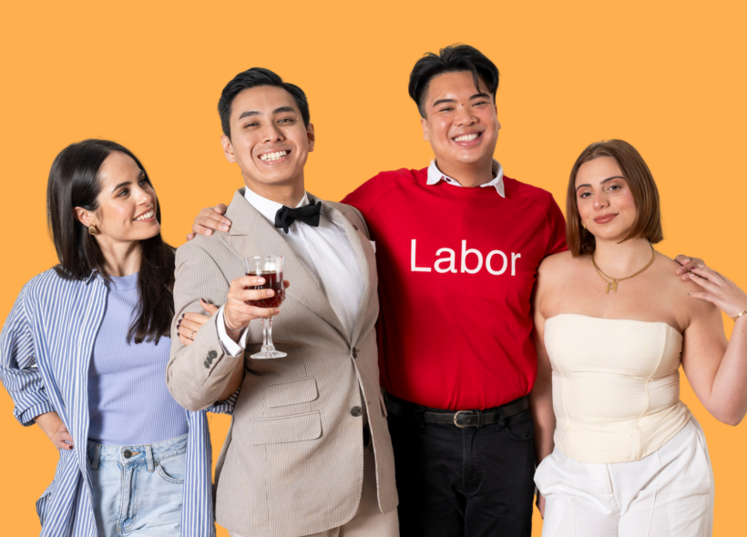 Four people smiling together against an orange background; one wears a “Labor” shirt, another holds a glass of red wine.