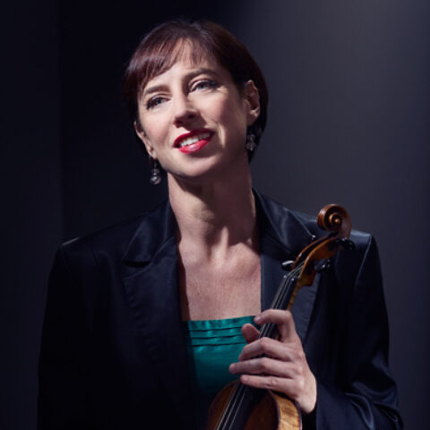 Madeleine Easton sits against a black background with a violin