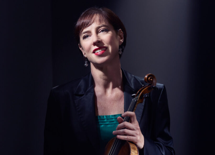 Madeleine Easton sits against a black background with a violin