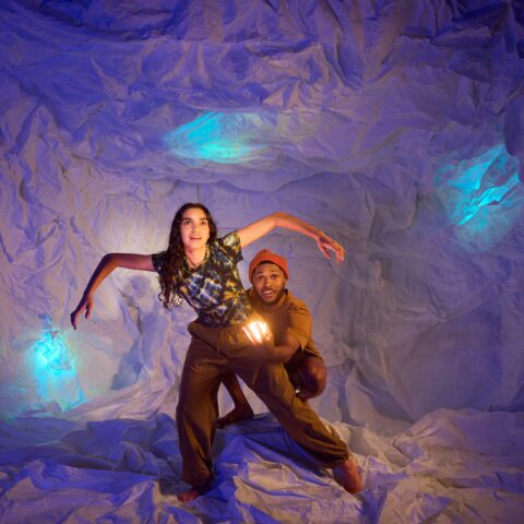 A man and woman explore a cave surrounded by glowing blue lights 