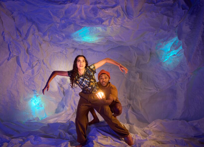 A man and woman explore a cave surrounded by glowing blue lights 