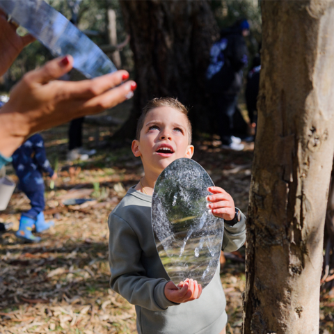 Forest production photo: Sarah Walker. A child holds a round mirror and gazes up to the sky.