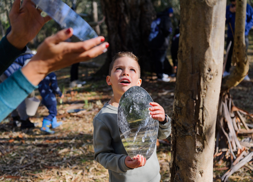 Forest production photo: Sarah Walker. A child holds a round mirror and gazes up to the sky.