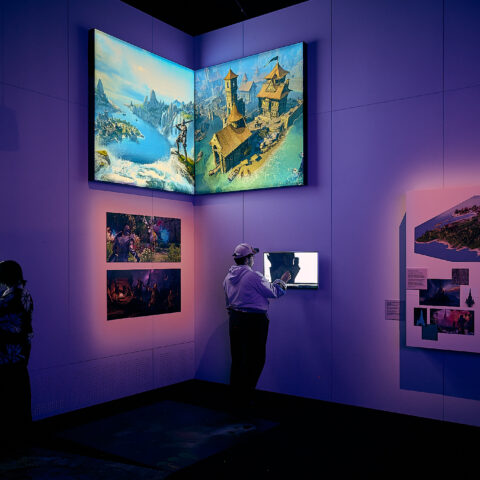 Two visitors experiencing the Game Worlds exhibition, interacting with screens on the wall.