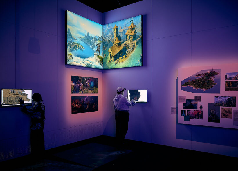 Two visitors experiencing the Game Worlds exhibition, interacting with screens on the wall.